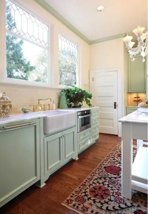 a mint farmhouse kitchen with shaker cabinets, white stone countertops, a bold printed rug and a vintage chandelier