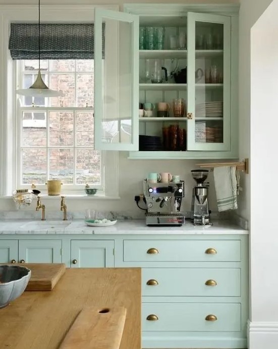 a mint green kitchen with white stone countertops, brass handles, a window to bring some natural light in