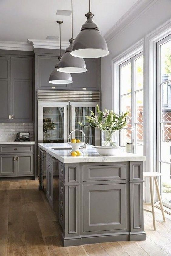 a modern farmhouse kitchen in grey with shaker style cabinets, a white subway tile backsplash, white marble countertops, grey pendant lamps