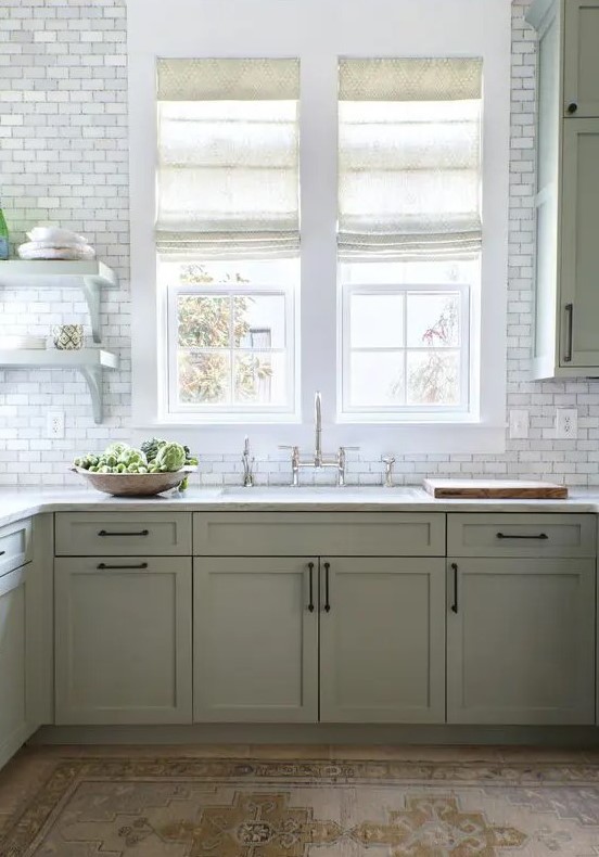 a modern farmhouse kitchen in sage green, with shaker cabinets, white stone countertops, white marble tiles and vintage fixtures