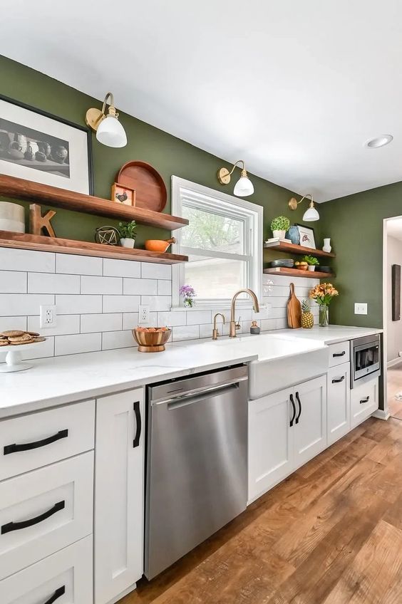 a modern farmhouse kitchen with green walls, white tiles, white cabinets and stone countertops, gold sconces