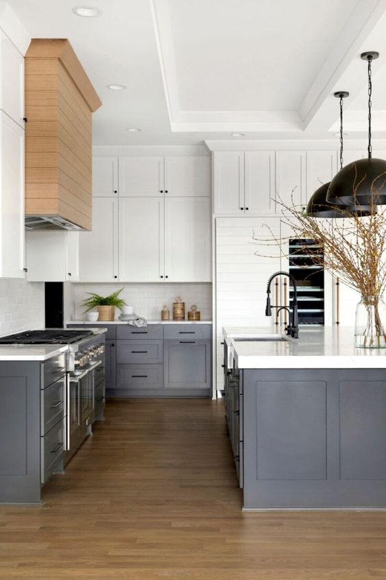 a modern farmhouse kitchen with white upper cabinets, dark grey lower ones, white countertops and a backsplash, black pendant lamps