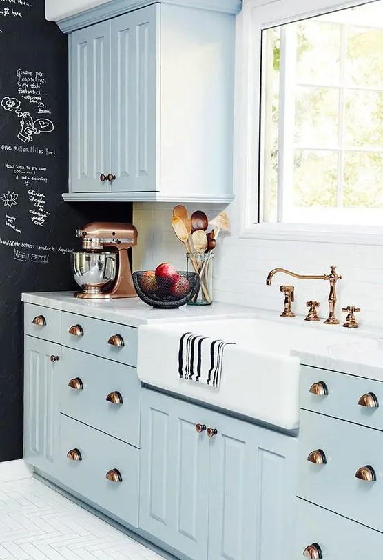 a pastel blue famrhouse kitchen with shaker cabinetry, a white stone countertop and a white tile backsplash plus a chalkboard wall