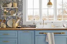 a pretty blue kitchen with a grey floral wallpaper wall and touches of gold and stained wood is vintage chic
