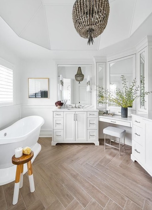 a refined bathroom with a wood look tile floor, a chic vanity, a tub, a beaded pendant lamp, a floating makeup vanity and a stool