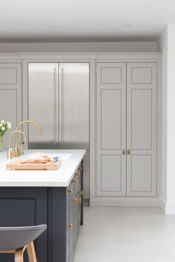 a refined kitchen in dove grey, with shaker cabinets, a navy kitchen island, a white stone countertop and some gold knobs and handles