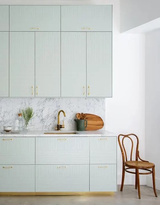 a refined light green kitchen with geo facades, a white marble backsplash and countertops plus gold fixtures