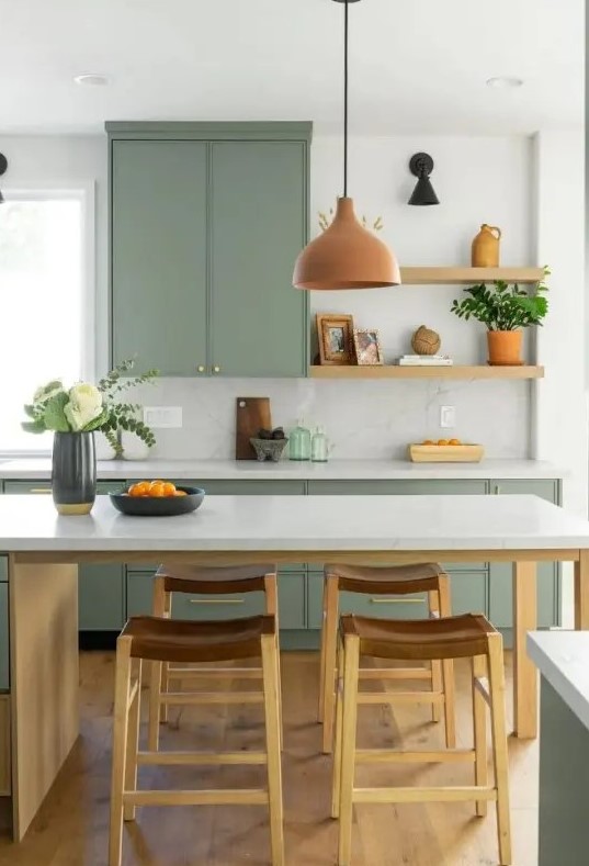 a sage green kitchen with open shelves and only lower cabinets, a kitchen island that doubles as a dining table