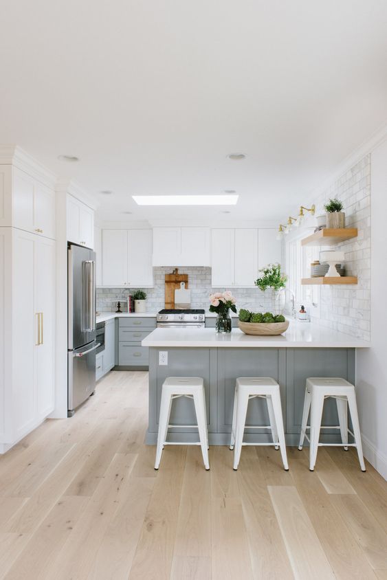 a serene kitchen with white upper cabinets and light grey lower ones, a large kitchen island, open shelves and white stools