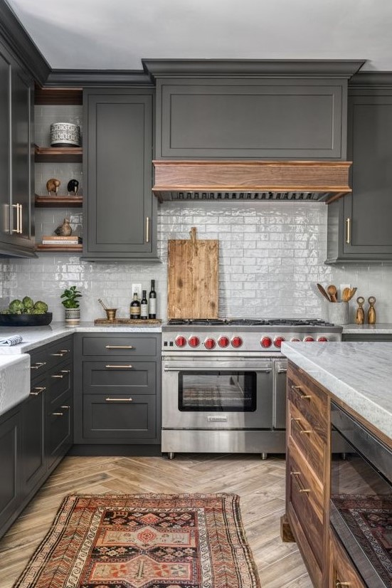 a slate grey kitchen with shaker cabinets, white skinny tiles, a wooden kitchen island and a wooden hood plus a bold rug