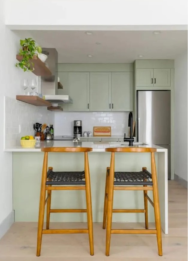 a small and cool sage green kitchen with shaker cabinets, white stone countertops and a white subway tile backsplash, black handles for a modern touch