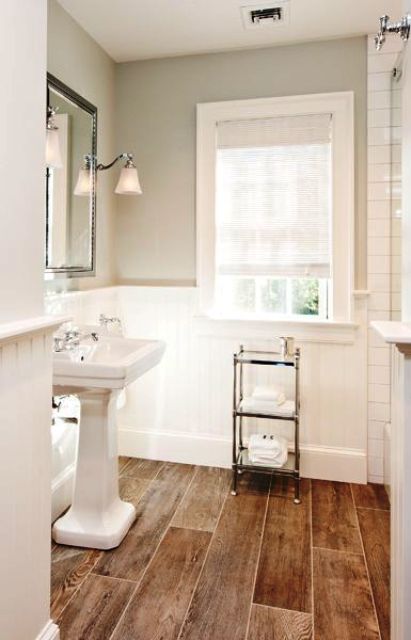 a small and lovely bathroom with light grey walls and paneling, a wood tile floor, a free-standing sink and a shower space