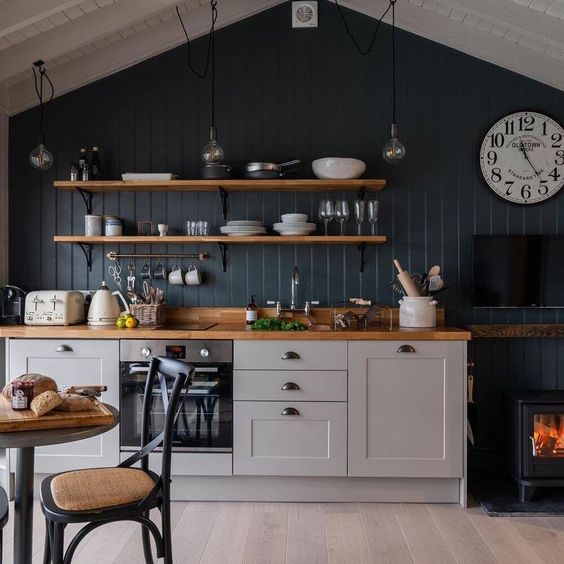 a small pretty kitchen with grey cabinets, a navy accent wall, open shelves, butcherblock countertops and a small hearth