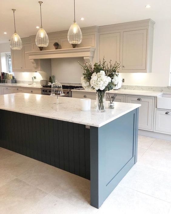 a sophisticated kitchen with dove grey shaker cabinets, a navy kitchen island, white stone countertops and cool pendant lamps