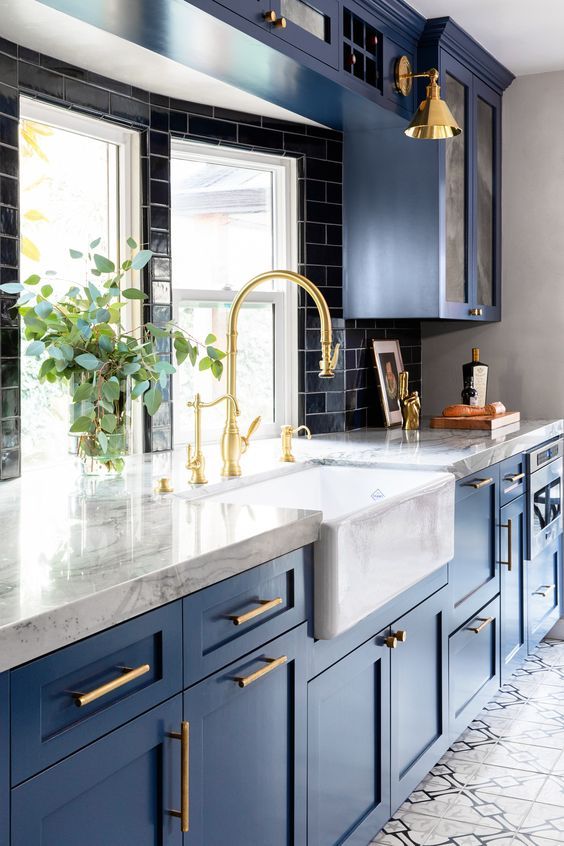 a stunning traditional kitchne in blue, with white stone countertops, a black tile backsplash and gold touches