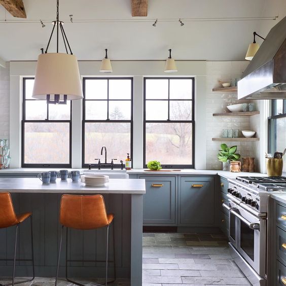 a stylish blue and grey kitchen with only lower cabinets, corner shelves, a cooker, a grey kitchen island, orange leather stools