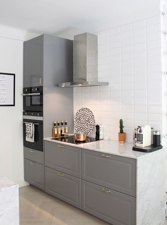 a stylish contemporary space with grey cabinets, a white tile backsplash and a stainless steel hood looks airy