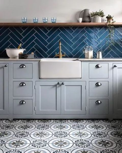 a stylish kitchen with dove grey cabinets, a navy herringbone tile backsplash, an open shelf, printed tiles on the floor