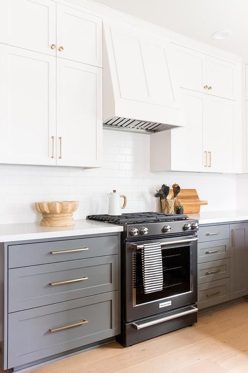 a stylish kitchen with white upper cabinets and grey lower ones, a white subway tile backsplash and white countertops plus gold handles