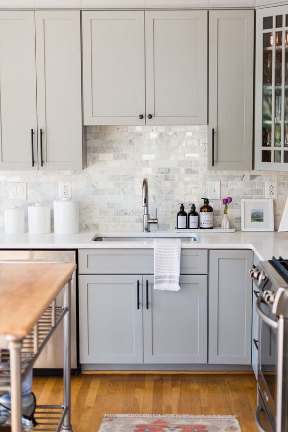 a stylish light grey kitchen with white countertops, a white marble tile backsplash in modern farmhouse style