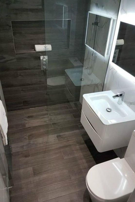 a stylish modern bathroom clad with marble and wood look tiles looks refined, with a lit up mirror, white appliances and a niche for storage