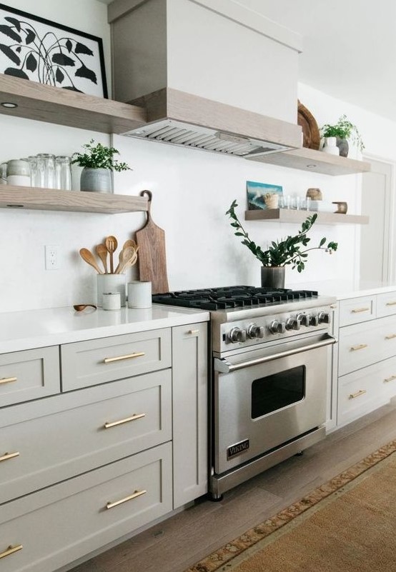 a stylish neutral kitchen in creamy and dove grey cabinets, wooden floating shelves and a white hood