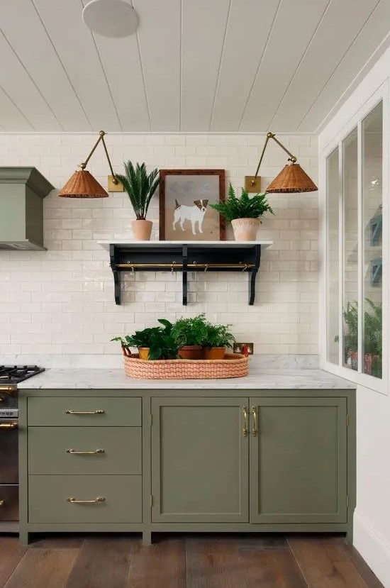 a stylish olive green farmhouse kitchen with shaker cabinets, a matching hood, a white subway tile backsplash, an open shelf, woven sconces