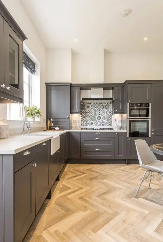 a stylish slate grey kitchen with shaker style cabinets, white countertops, a printed tile backsplash and built-in lights