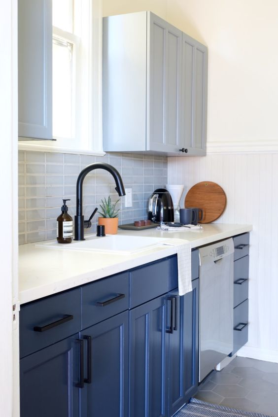 a stylish small kitchen with dove grey and bold blue cabinets, a grey tile backsplash, a white stone countertop