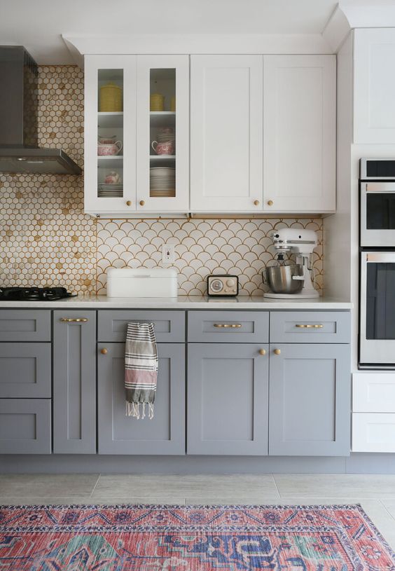 a stylish two-tone kitchen with upper white and lower grey cabinets, a penny and scallop tile backsplash, a bold rug