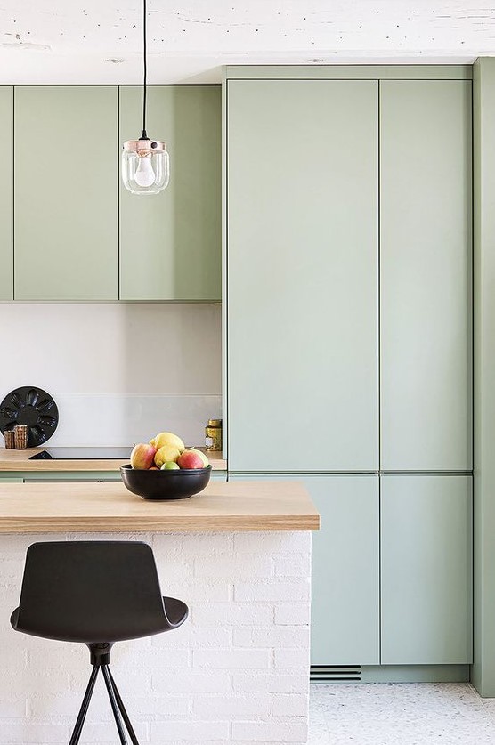 a subtle minimalist kitchen with sleek mint cabinets, a white kitchen island, butcherblock countertops and pendant bulbs