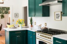 a super bold kitchen with teal cabinets, a white penny tile backsplash and countertops plus gold touches here and there