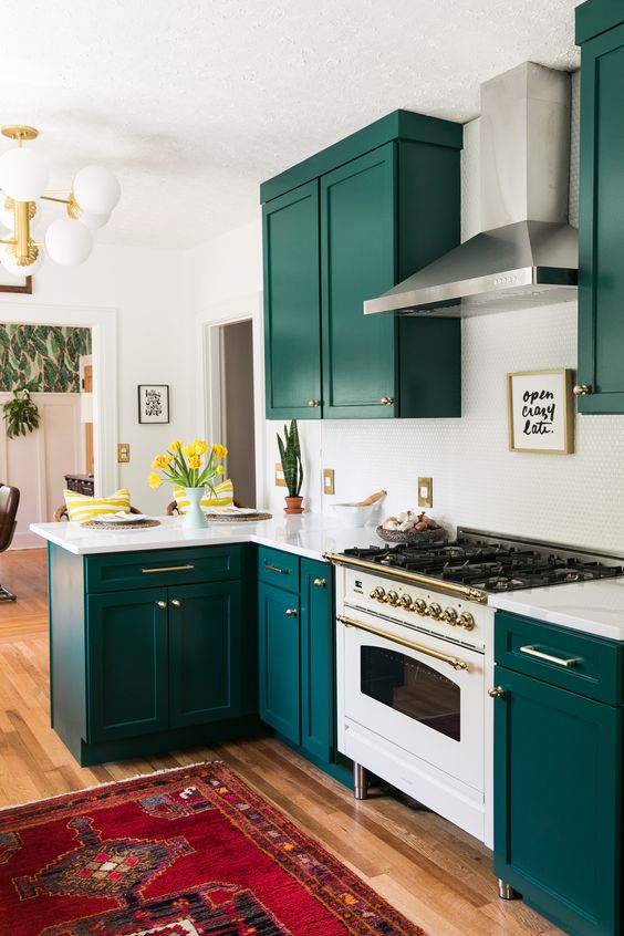 a super bold kitchen with teal cabinets, a white penny tile backsplash and countertops plus gold touches here and there