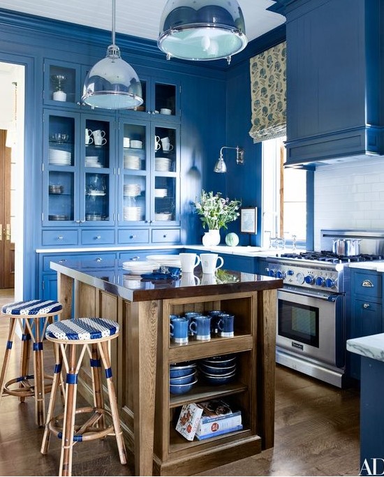 a super bright blue kitchen with a white subway tile backsplash, pendant lamps, a printed shade and a wooden kitchen island