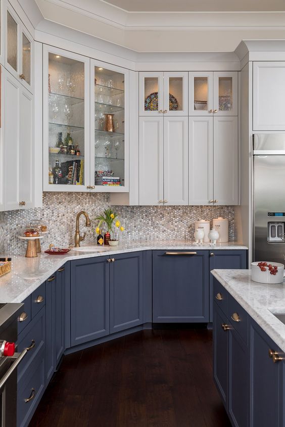 a traditional kitchen with blue lower cabinets, neutral upper ones, a mother of pearl bacskplash and touches of gold