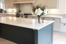 a vintage dove grey kitchen with a statement navy kitchen island and white sone countertops plus glass pendant laps