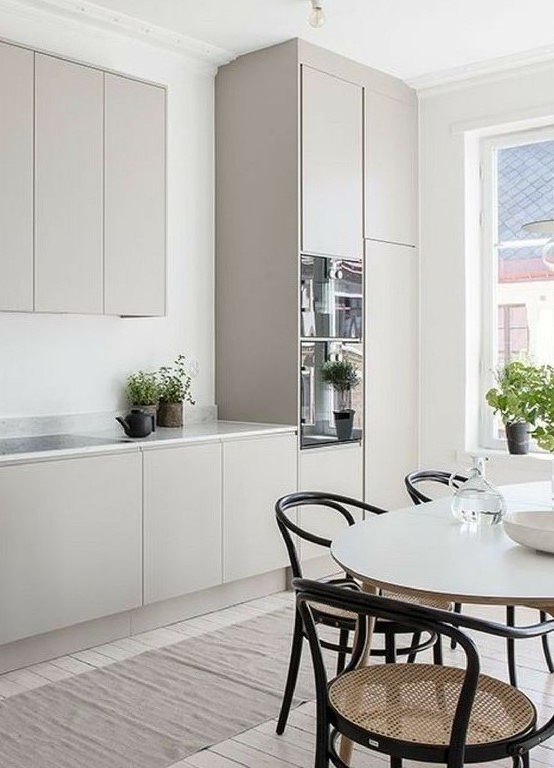 a welcoming Scandinavian kitchen with plain grey cabbinets, a white marble countertop, an oval table and cool retro rattan chairs