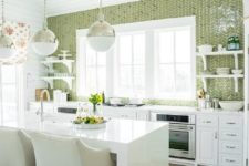 a welcoming kitchen with white cabinets, a white stone kitchen island, a green tile wall and touches of metallic shades