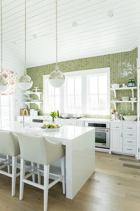 a welcoming kitchen with white cabinets, a white stone kitchen island, a green tile wall and touches of metallic shades