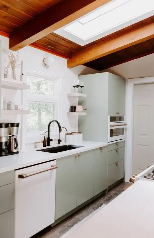 a welcoming mid-century modern kitchen in light green, a skylight, a stained wood ceiling, white stone countertops