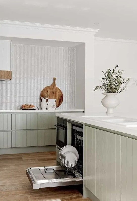 an airy contemporary kitchen with lower sage green slatted cabinets, a white skinny tile backsplash and white stone countertops