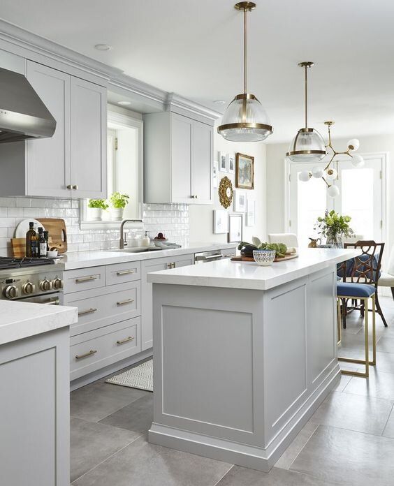 an airy dove grey kitchen with shaker cabinets, a white subway tile backsplash and white countertops and chic pendant lamps