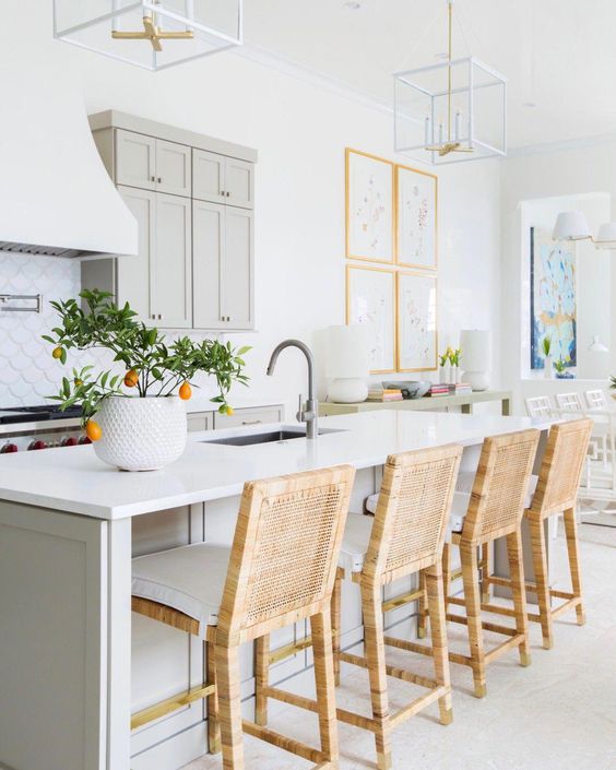 an airy kitchen with dove grey cabinets and a kitchen island, white stone countertops, wicker stools and frame chandeliers