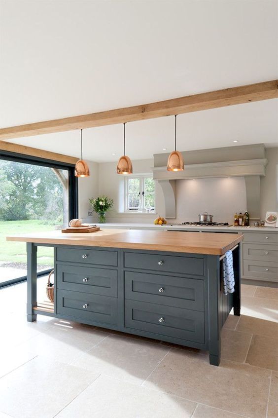 an elegant kitchen with grey cabinets, a large grey hood, a navy kitchen island with a butcheblock countertop and copper pendant lamps