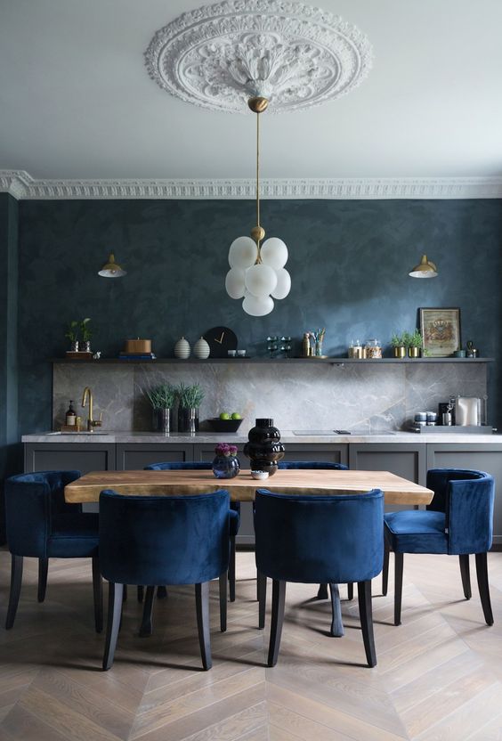 an exquisite kitchen with grey lower cabinets, an open shelf, a grey stone backsplash and countertops, a stained table and navy chairs