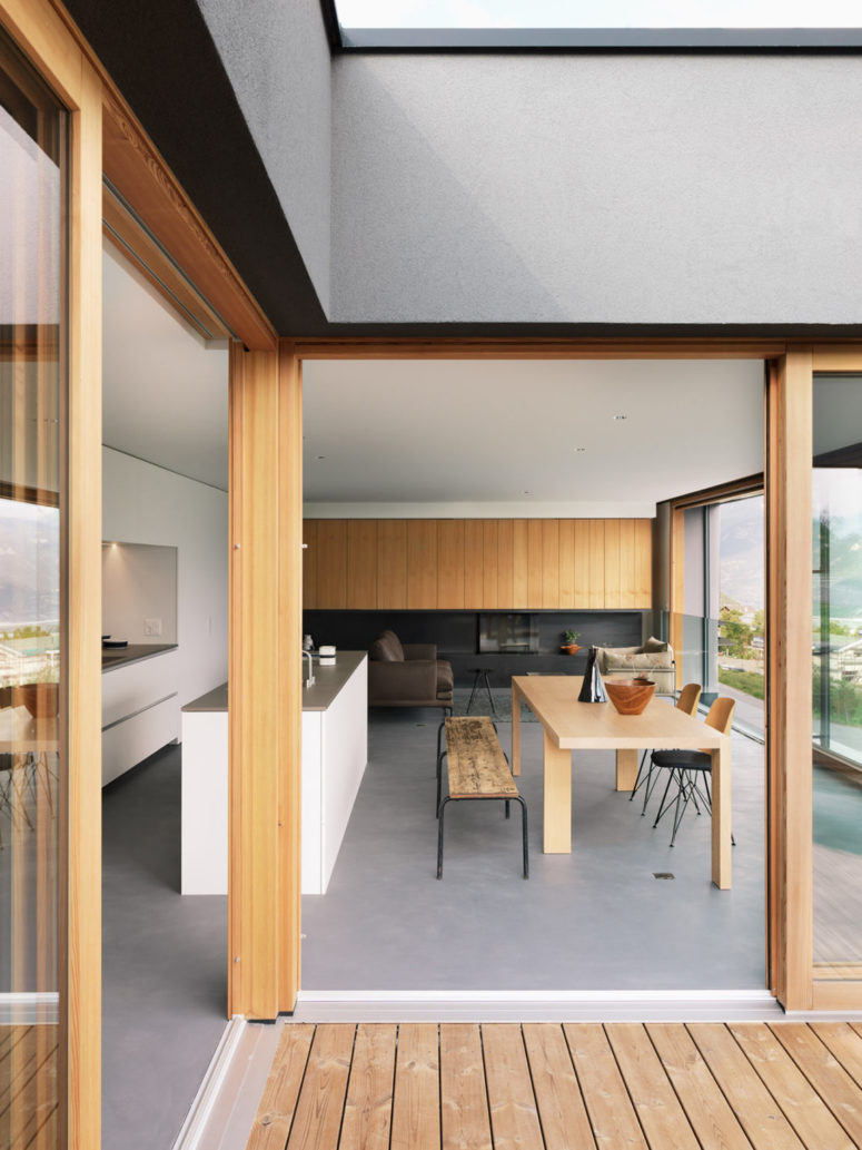 The main space is an open layout with a white minimalist kitchen with concrete countertops, a dining zone with rustic benches and a living room