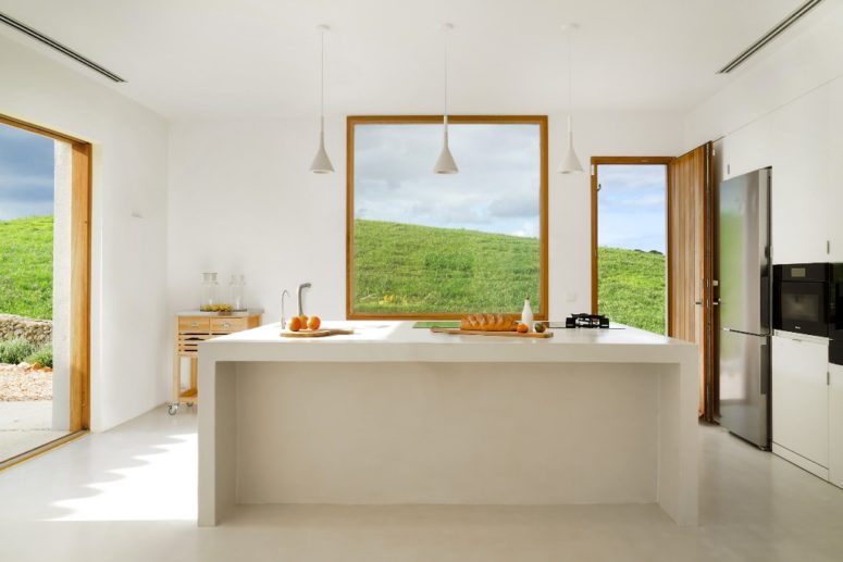 The kitchen is all-white, with windows and openings that add natural colors to the space and a large kitchen island