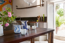 04 The kitchen is done with metal cabinets, wooden countertops, a bright artwork, a rich-stained table and bright porcelain