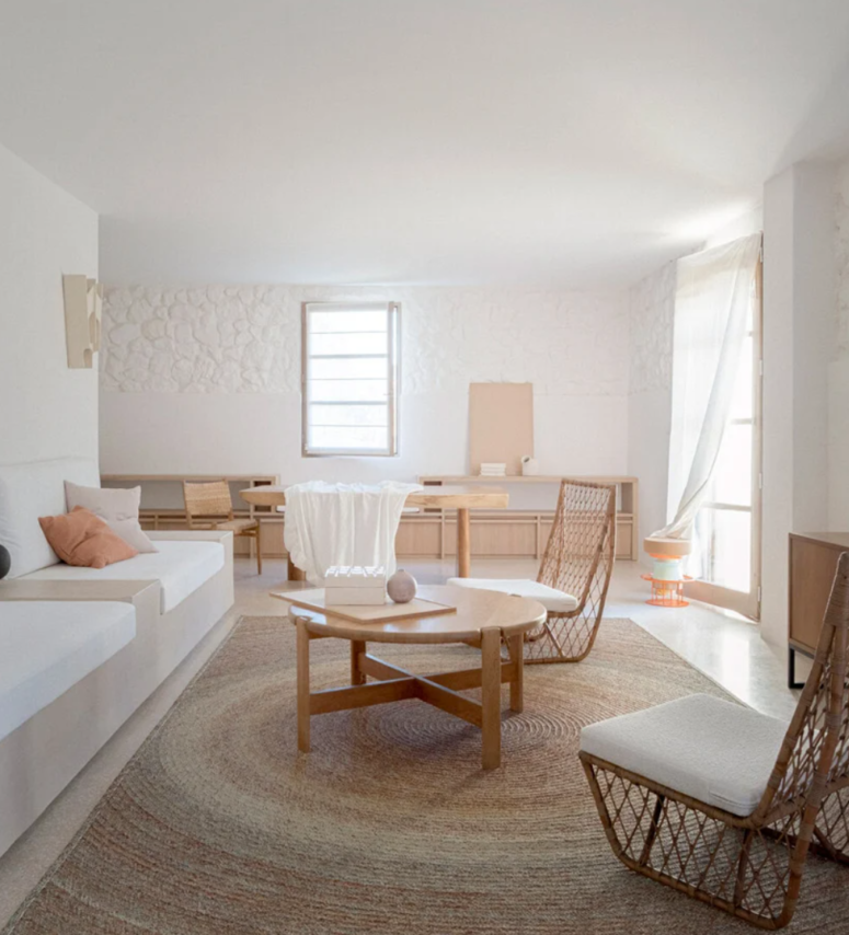 The living room features pure white walls with stone parts, simple wooden and wicker furniture, minimalist sofas and airy and light textiles
