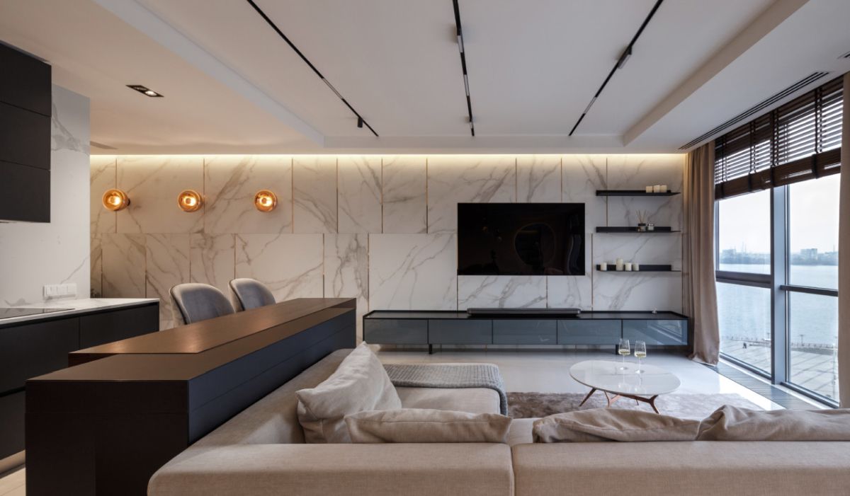 The living room is done with comfortable modern furniture, white marble on the wall and a dark TV unit